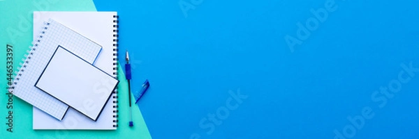Fototapeta Banner of back to school concept. Stack of white spiral notebook, notepad and notepaper with pen, on a blue and aqua colorful background. School office supplies. Top view, flat lay