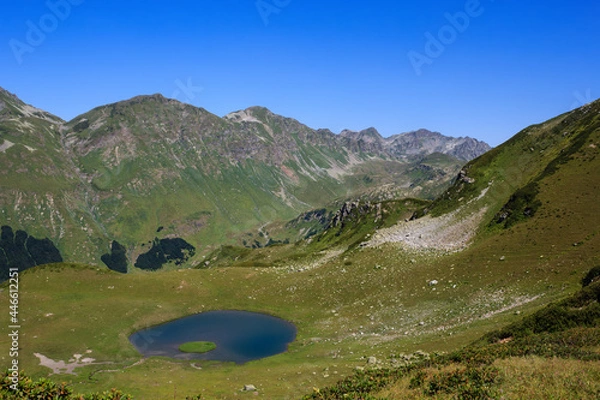 Obraz The Main Caucasian Ridge and blue mountain lake surrounded with grass and flowers of the alpine meadows