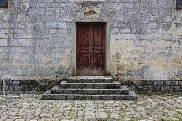 Fototapeta obsolete brown wooden door and with lock stone bricks steps in the front of ancient building