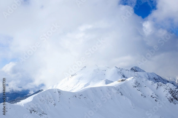 Fototapeta building ot the top of snowy mountain ridge in the sunligt and clouds