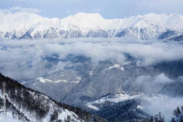 Fototapeta road to ski resort hotels and high mountains covered with snow and clouds in Sochi