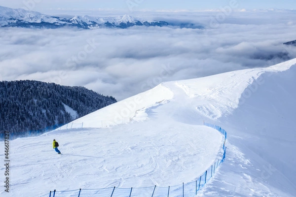 Fototapeta snowboarder on his descent on the trail in mountain ski resort and forest clouds behind