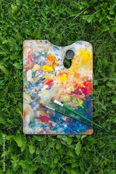 Fototapeta Real Artist's palette with multiple colors on the green  grass. Oil paints of different colors