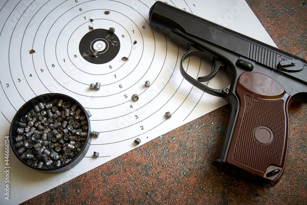 Obraz A sports pistol on the background of a target with bullet holes and lead bullets.