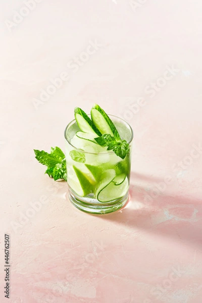 Fototapeta Fresh summer detox and refreshing drinks with cucumber, lime, mint on white wall background. Sunny day shadows from mocktail on pink surface.