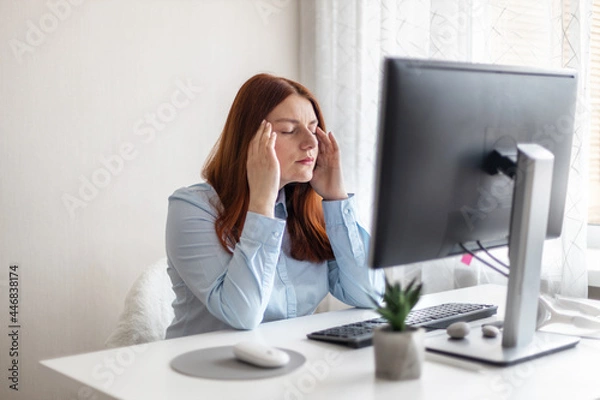 Fototapeta Young Caucasian women are stressed and tired from work at a white desk with a computer at home