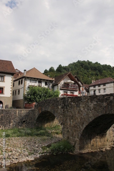Fototapeta Stone bridge over a river and typical houses with a cloudy sky in Otsagabia, Navarra