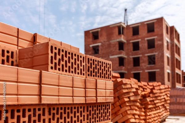 Obraz Stack of red clay brick on construction site on multistory building background.