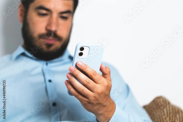 Fototapeta A man with a beard holds a mobile phone and looking in the screen business
