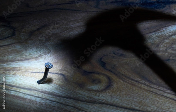 Obraz Hammer and nail. The shadow of the hammer hammers a nail into the board. The concept of threat, fear, danger. Light and shadow.