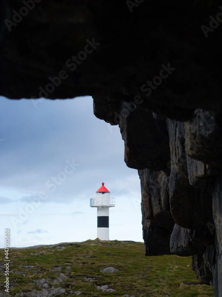 Fototapeta Lighthouse with rocks and cloudy sky