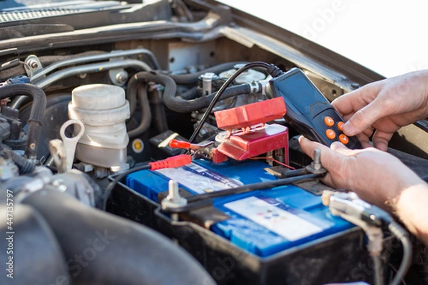 Obraz A man diagnoses a car battery with a tester, close-up. Battery repair and replacement