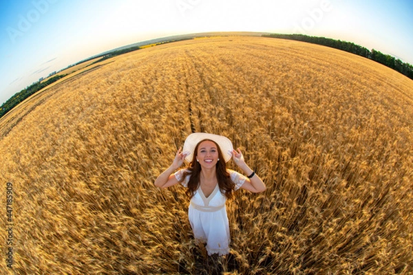 Fototapeta Happy woman stands in a wheat field in the summer against the background of a setting sun
