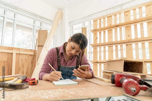 Obraz Portrait of females carpenter using mobile phone while checking list on the notebook
