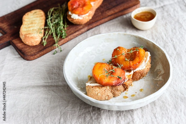 Fototapeta Summer Breakfast - toast (sandwich, bruschetta) with grilled peaches, cream cheese (ricotta, mascarpone), thyme and honey on beige linen tablecloth. Selective focus
