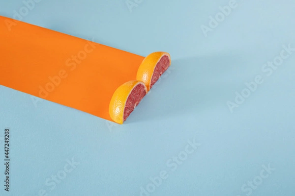 Fototapeta two half of red  grapefruit and orange paper with copy space against pastel blue background. abstract art. minimalism