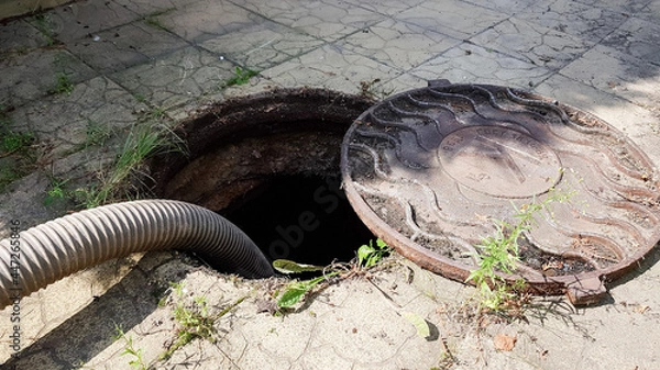 Obraz Open sewer manhole in the courtyard of a private house next to a fir tree. cleaning of the sewer