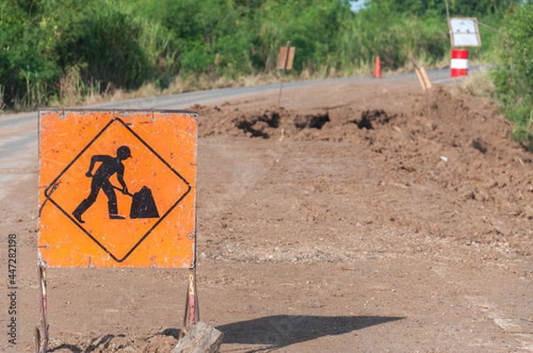 Fototapeta Znak ostrzegawczy drogi ma pracowników pracujących na powierzchni drogi. Droga wzdłuż kanału zawaliła się, gdy poziom wody był niski. i otrzymał wibracje z samochodu, powodując w ten sposób zawalenie się