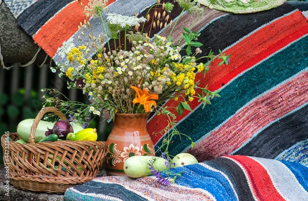 Obraz Summer still life with wildflowers and a basket of vegetables. Zucchini in a basket on the background of a decorative carpet