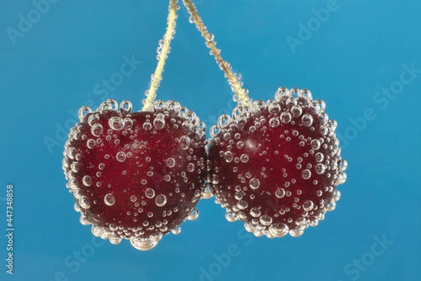 Obraz Two isolated red cherries in sparkling water with blue background