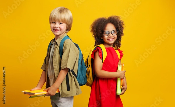 Fototapeta children with school backpacks are looking at the camera, holding books and pencils in their hands