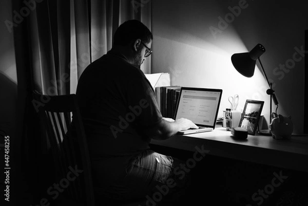 Fototapeta Man working in a dark home office with a laptop