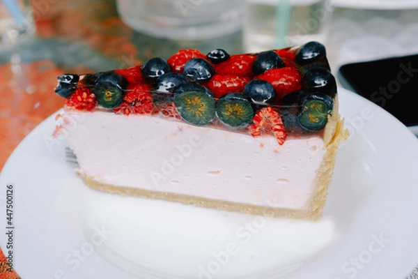 Fototapeta Close-up of a piece of berry cheesecake with blueberries and raspberries on a white plate. Photo for the menu of cafes, pastry shops. The concept of sweet food, pastry, recipes.