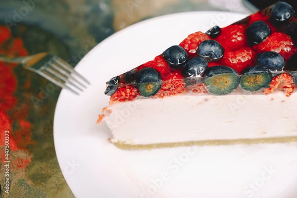 Fototapeta Close-up of a piece of berry cheesecake with blueberries and raspberries on a white plate. Photo for the menu of cafes, pastry shops. The concept of sweet food, pastry, recipes.