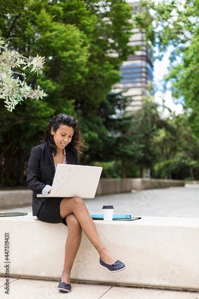 Fototapeta Young latin american woman using a laptop computer outdoors. Space for text.