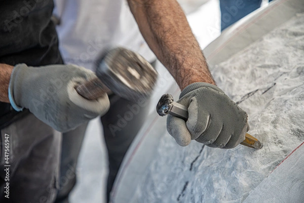 Fototapeta Detail of artist's hands sculpting marble with hammer and chisel