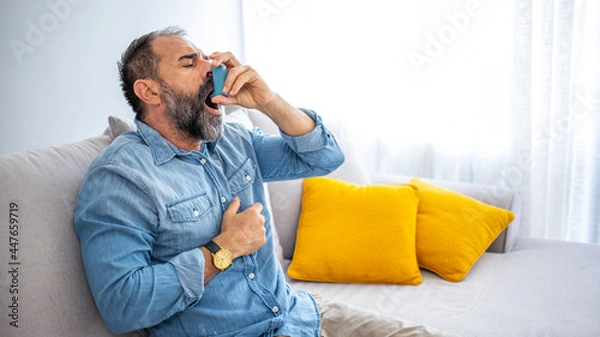 Fototapeta Cropped shot of a handsome mature man sitting alone at home and using an asthma pump. Man Inhaling Asthmatic Cure at Home. Mature man using medical inhaler to prevent shortness of breath