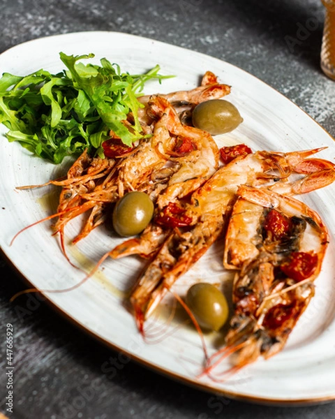 Obraz Fried langoustines served with olives and salad leaves. Grilled tasty langoustines on a white oval plate. Restaurant serving, horizontal orientation.