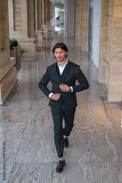 Fototapeta Young successful business man in black suit walking on the street near modern office building. 