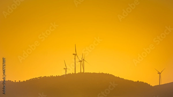 Fototapeta Landscape with wind turbines that produce electricity by rotating in the wind. Wind farm eco field. Eolic park with orange sky background.