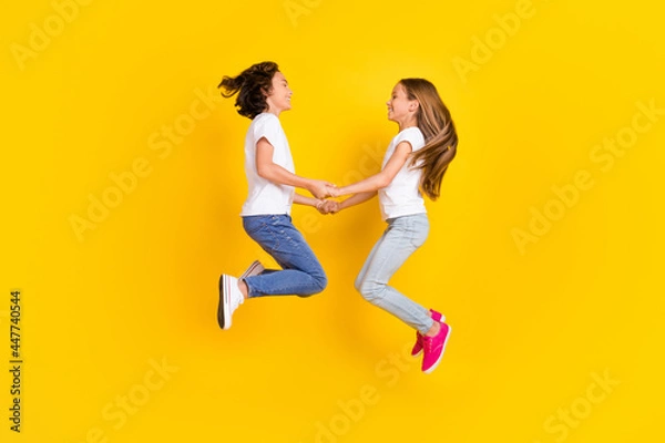 Fototapeta Full length body size view of two nice cheerful carefree kids jumping holding hands isolated over bright yellow color background