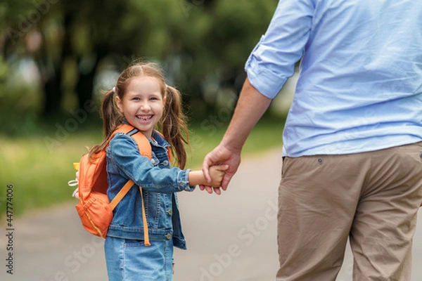 Fototapeta loving family. a caring dad accompanies a little girl with backpacks to school. The child smiles and looks over his shoulder. Close-up. Back to school. the first day of training