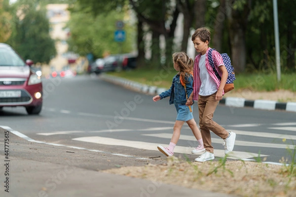 Fototapeta girl and boy with backpacks carefully cross road on pedestrian crossing on their way to school. Traffic rules. Walking path along zebra in city. concept of pedestrians crossing pedestrian crossing.