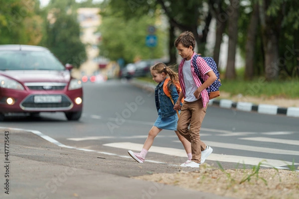 Fototapeta Dziewczyna i chłopiec z plecakami ostrożnie przekraczają drogę dla pieszych w drodze do szkoły. Zasady drogowe. Ścieżka spaceru wzdłuż Zebry w mieście. Pojęcie pieszych przekraczających skrzyżowanie pieszych.