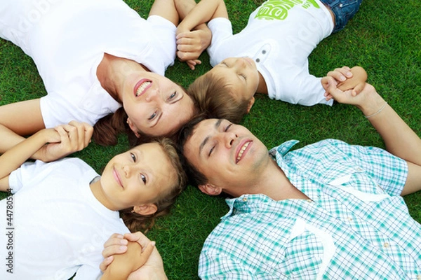 Obraz Семья с двумя детьми лежит на траве, вид сверху