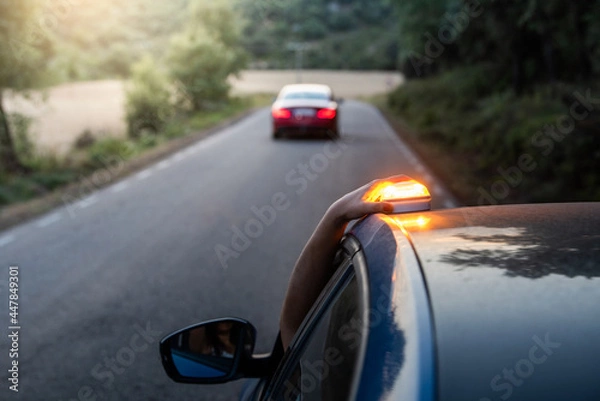Fototapeta hand placing the new V16 emergency light, which replaces the emergency triangles, broken blue vehicle stopped on the road and with another car in the background
