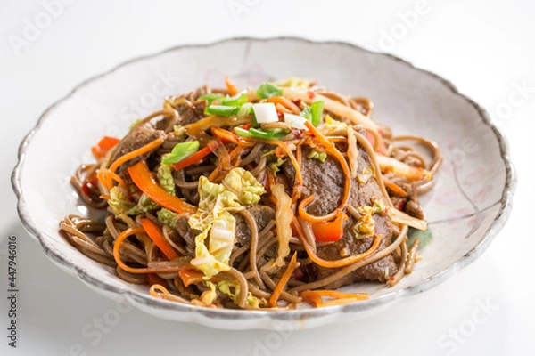 Fototapeta Soba noodles with beef, carrots, onions and sweet peppers isolated on white background