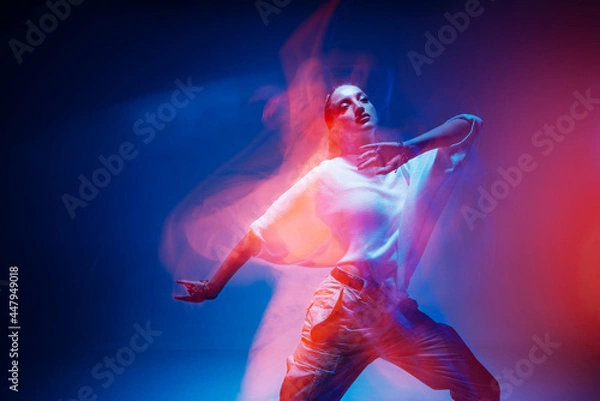 Obraz Dancing young mixed race girl enjoying moving in colorful neon studio light. Long exposure. Ethnic fiery dance