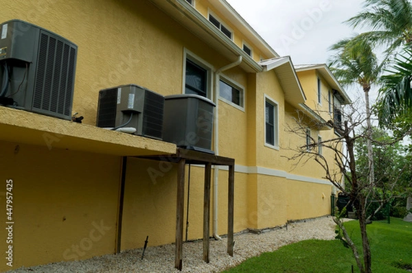 Obraz View of a long yellow and white building showing air handler units or air conditioners on exterior of building in florida with palm trees