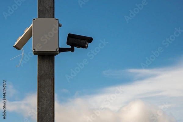 Fototapeta Security camera on a pole. Cloudy sky in the background