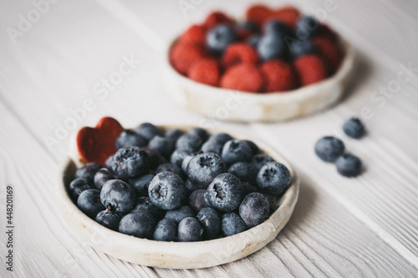 Fototapeta raspberries and blueberries in small ceramic bowls with red heart decor