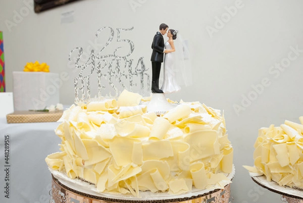 Fototapeta 25 year wedding anniversary topper with bride and groom on top of a white cake with shaved with chocolate.