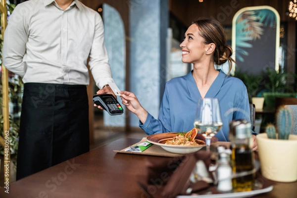 Fototapeta Beautiful young woman paying for her order with a credit card in a restaurant.