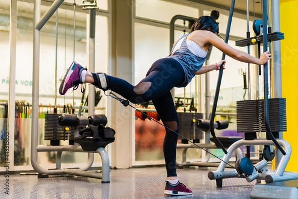 Obraz young hispanic latina doing gluteus with kickbacks in a rope machine. cable machine.