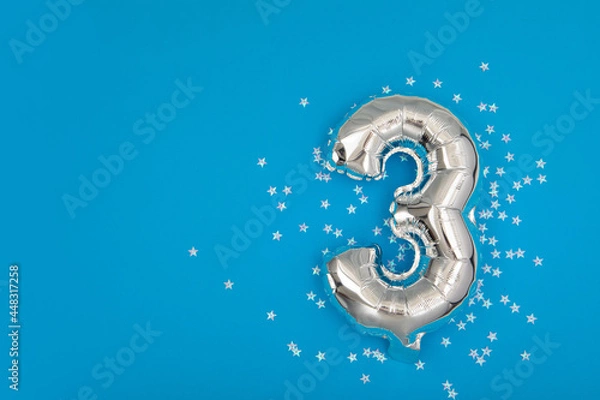 Fototapeta Silver balloon 3 on a blue background with confetti stars. Number three 3. Holiday Party Decoration or postcard concept with top view on blue background