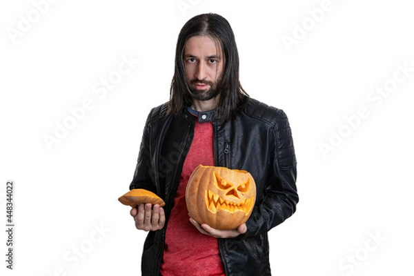 Fototapeta A man with a beard and long hair in a black jacket with a pumpkin in his hands posing on a white background. Various poses and emotions. Halloween concept. 